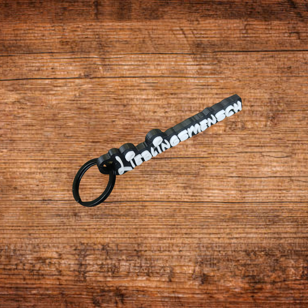 Schlüsselanhänger mit schwarzem Ring und weißem Schriftzug auf schwarzem Band.