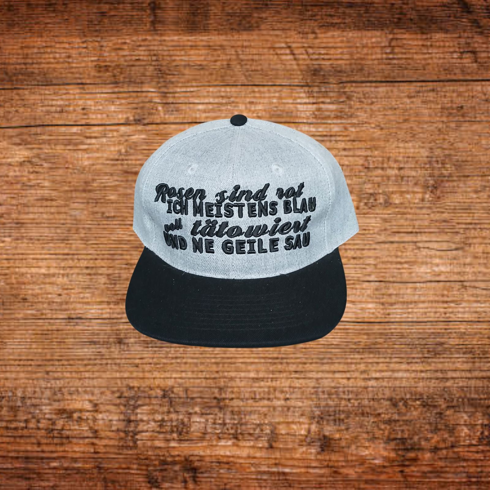 Snapback-Kappe mit hellgrauem Oberteil und schwarzem Schirm, mit Druckschrift vorn.